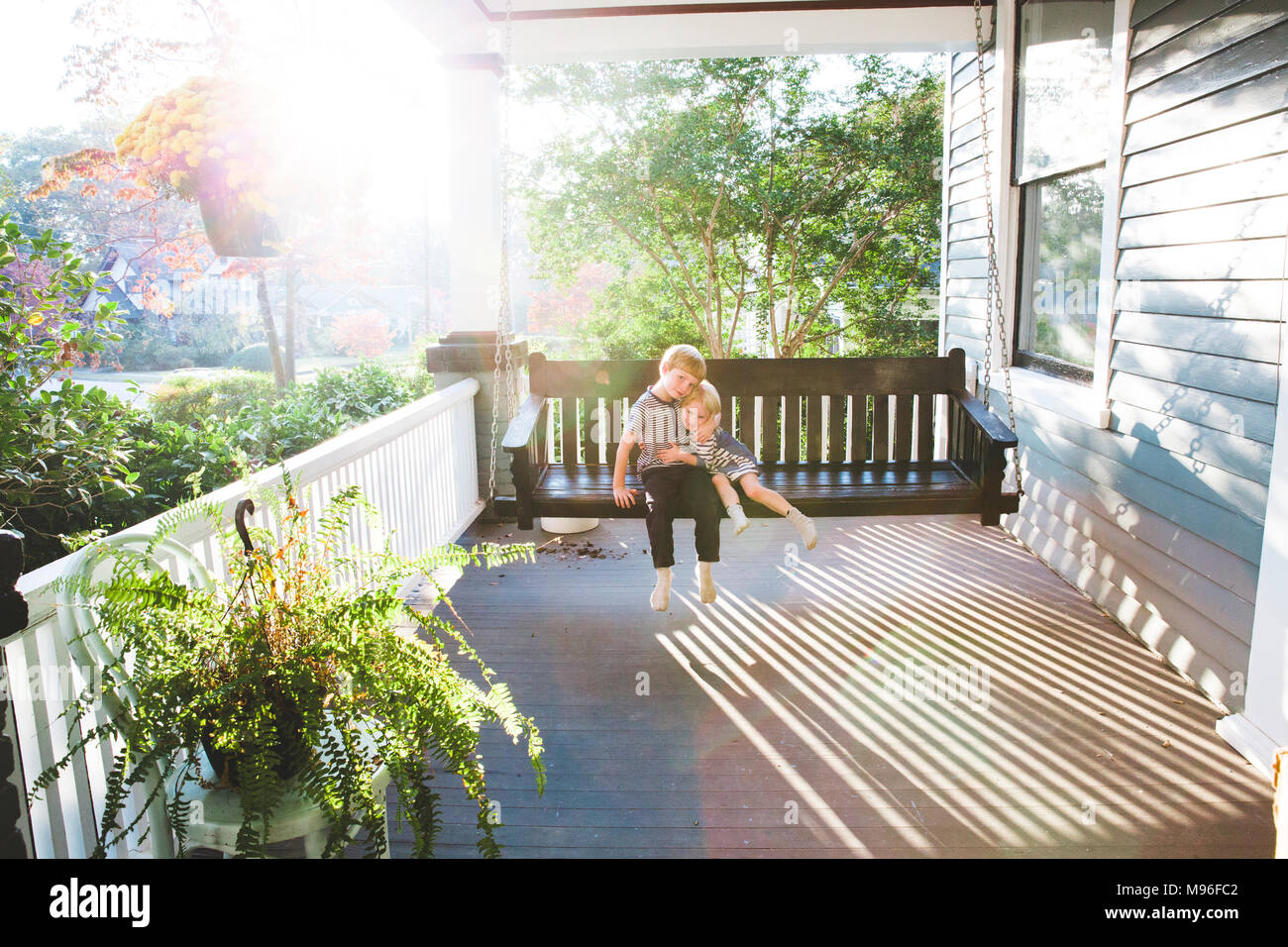 Children hugging on swinging bench on porch Stock Photo