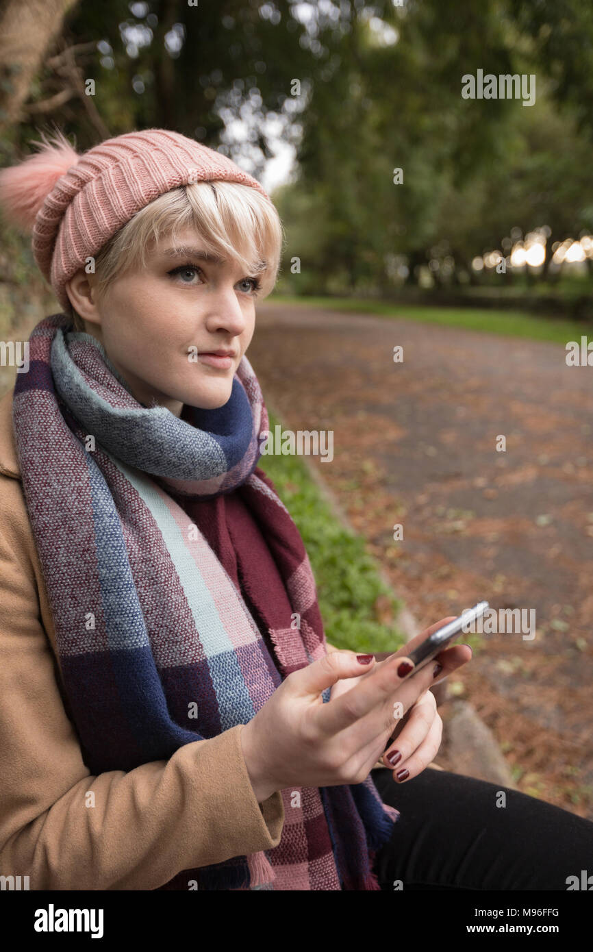 Woman in warm clothing using mobile phone at park Stock Photo