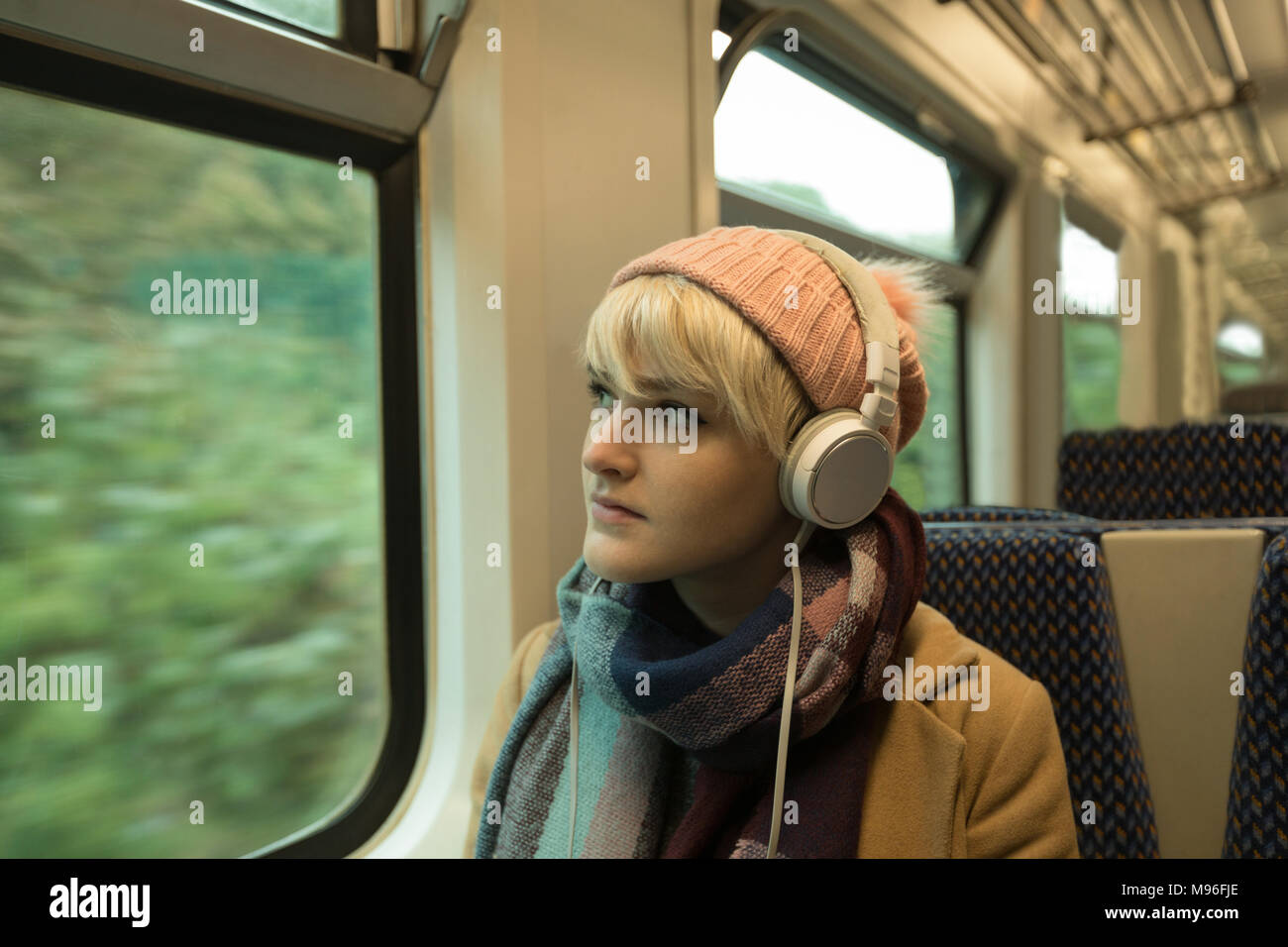 Young woman in warm clothing listing to music on headphones Stock Photo