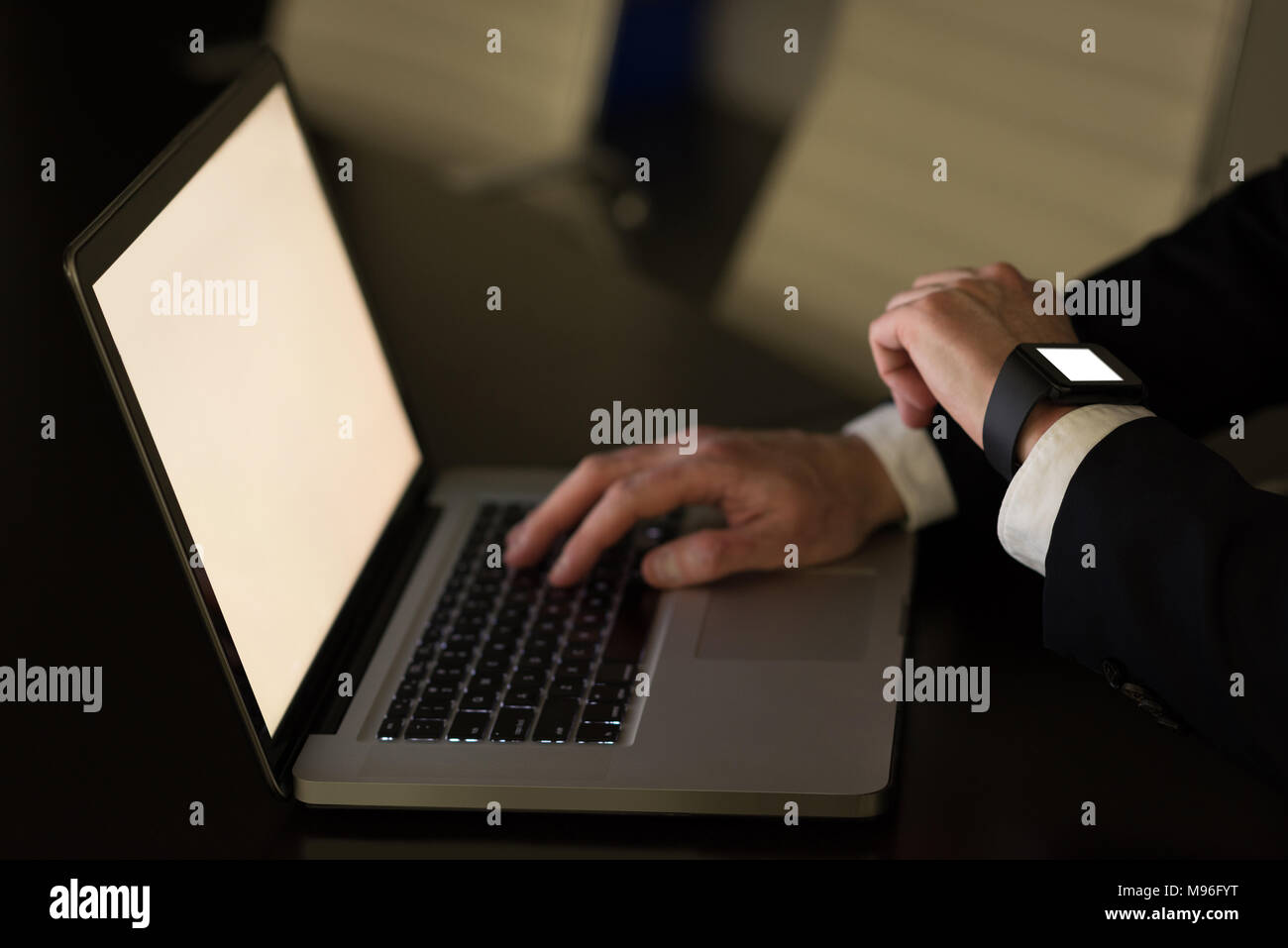 Businessman checking time while using laptop at desk Stock Photo