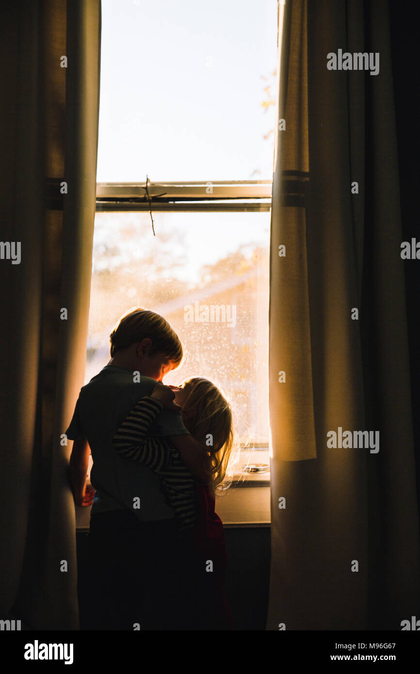 Children hugging next to dim window space Stock Photo