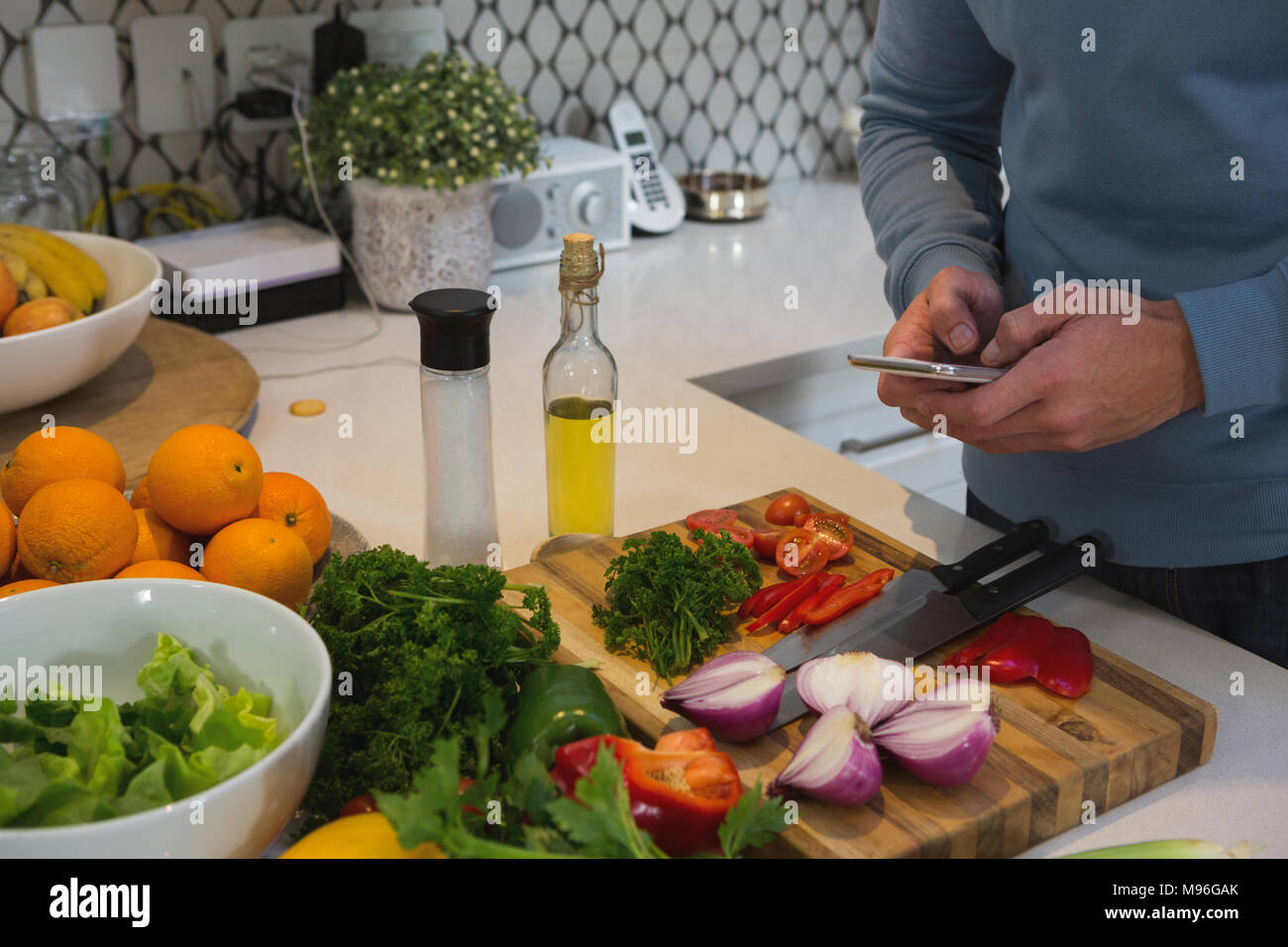 Man using mobile phone while cutting vegetables in kitchen Stock Photo