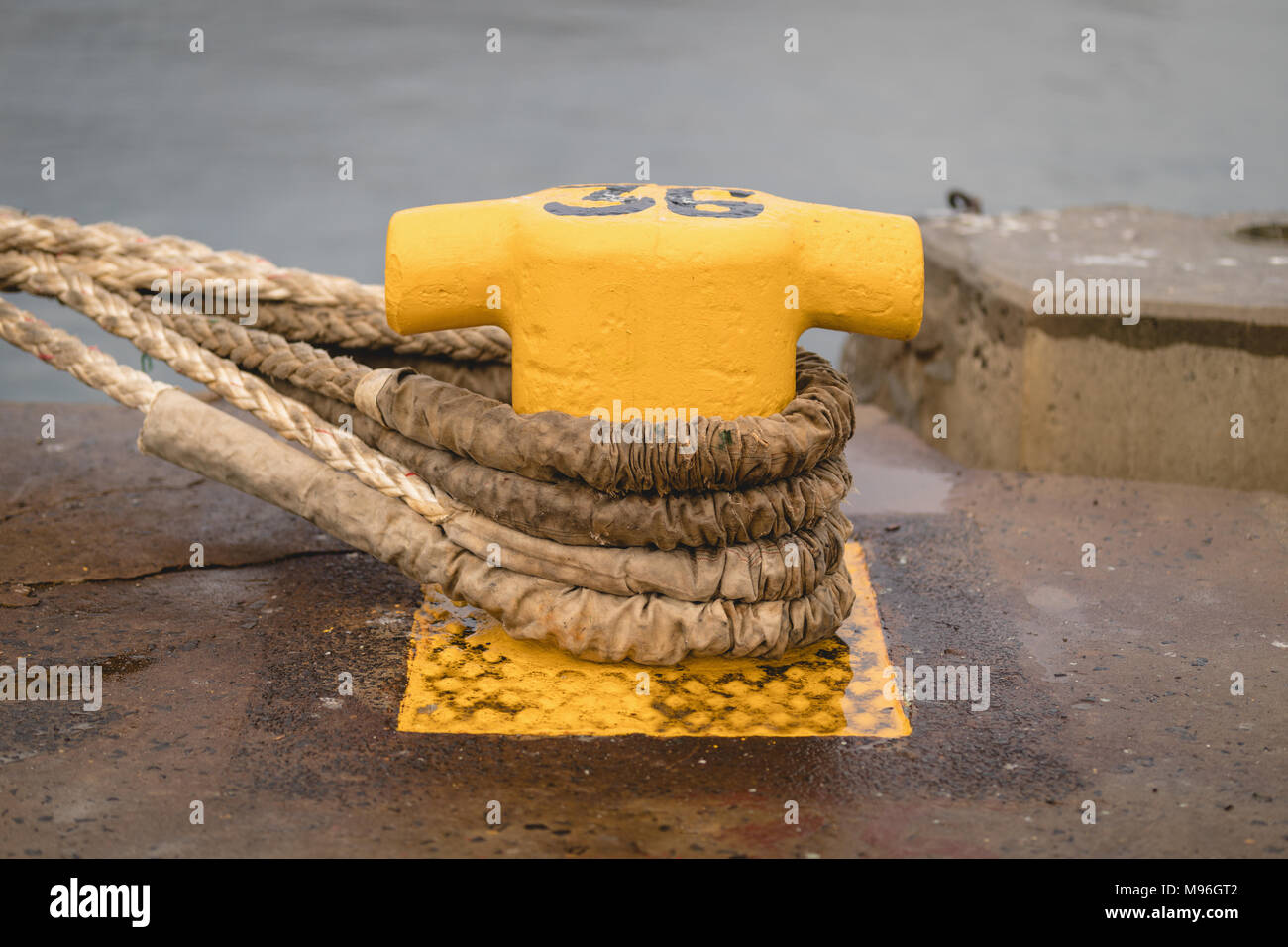 Old mooring bollard with rope tied on pier Stock Photo