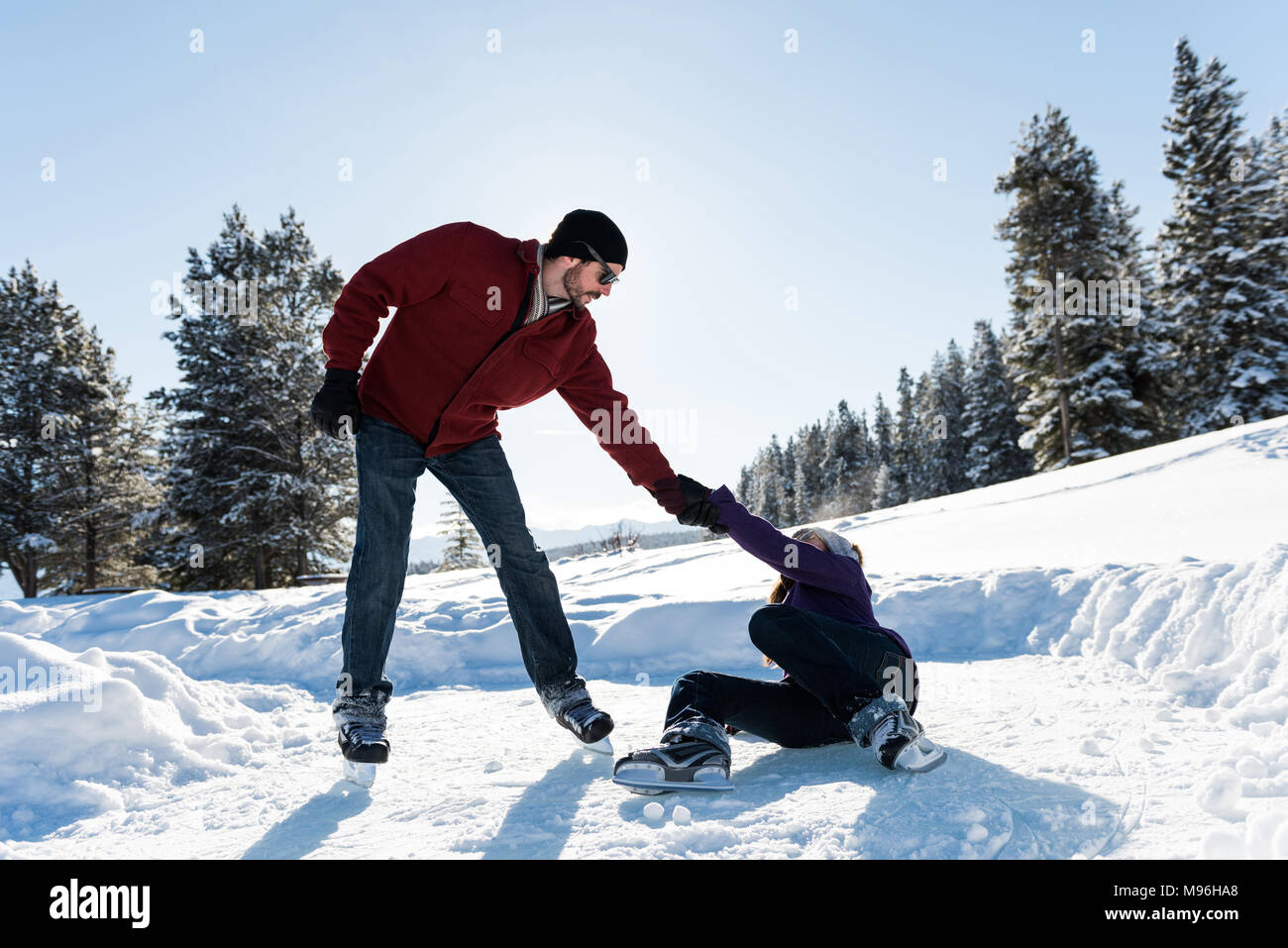 Man helping woman to rise up while skating in snowy landscape Stock Photo