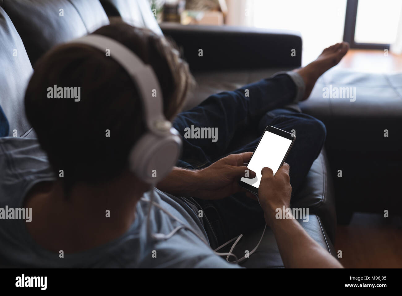 Man using mobile phone with headphones in living room Stock Photo