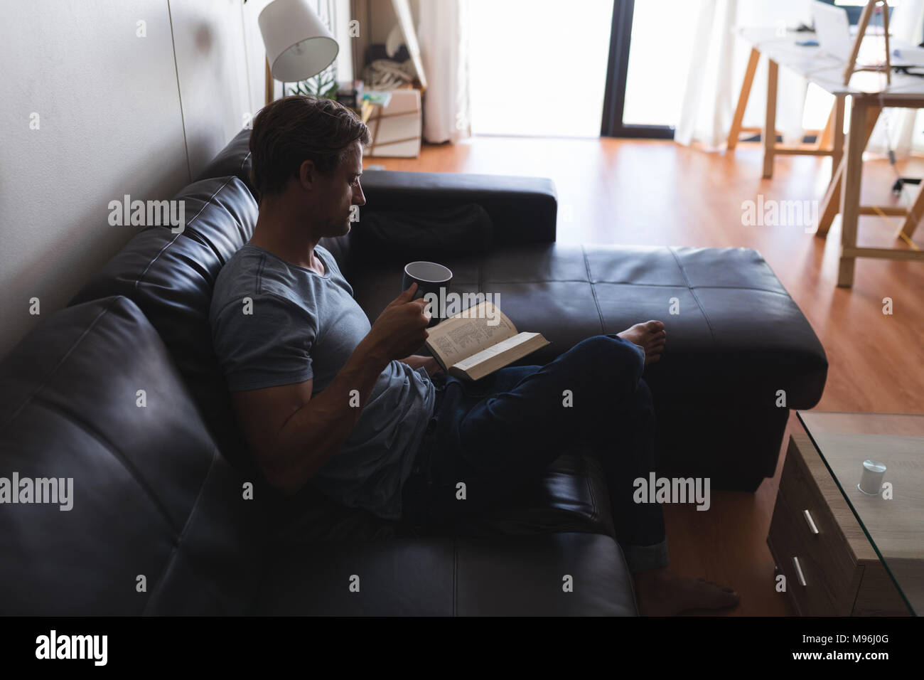 Man having coffee while reading a book in living room Stock Photo