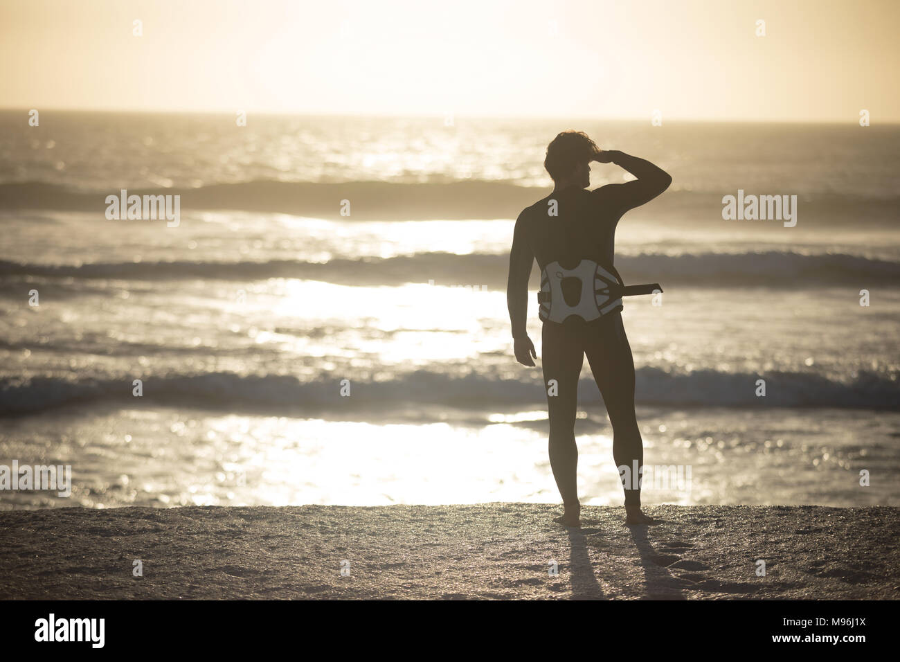 Male surfer standing in swimsuit and waist harness at beach Stock Photo