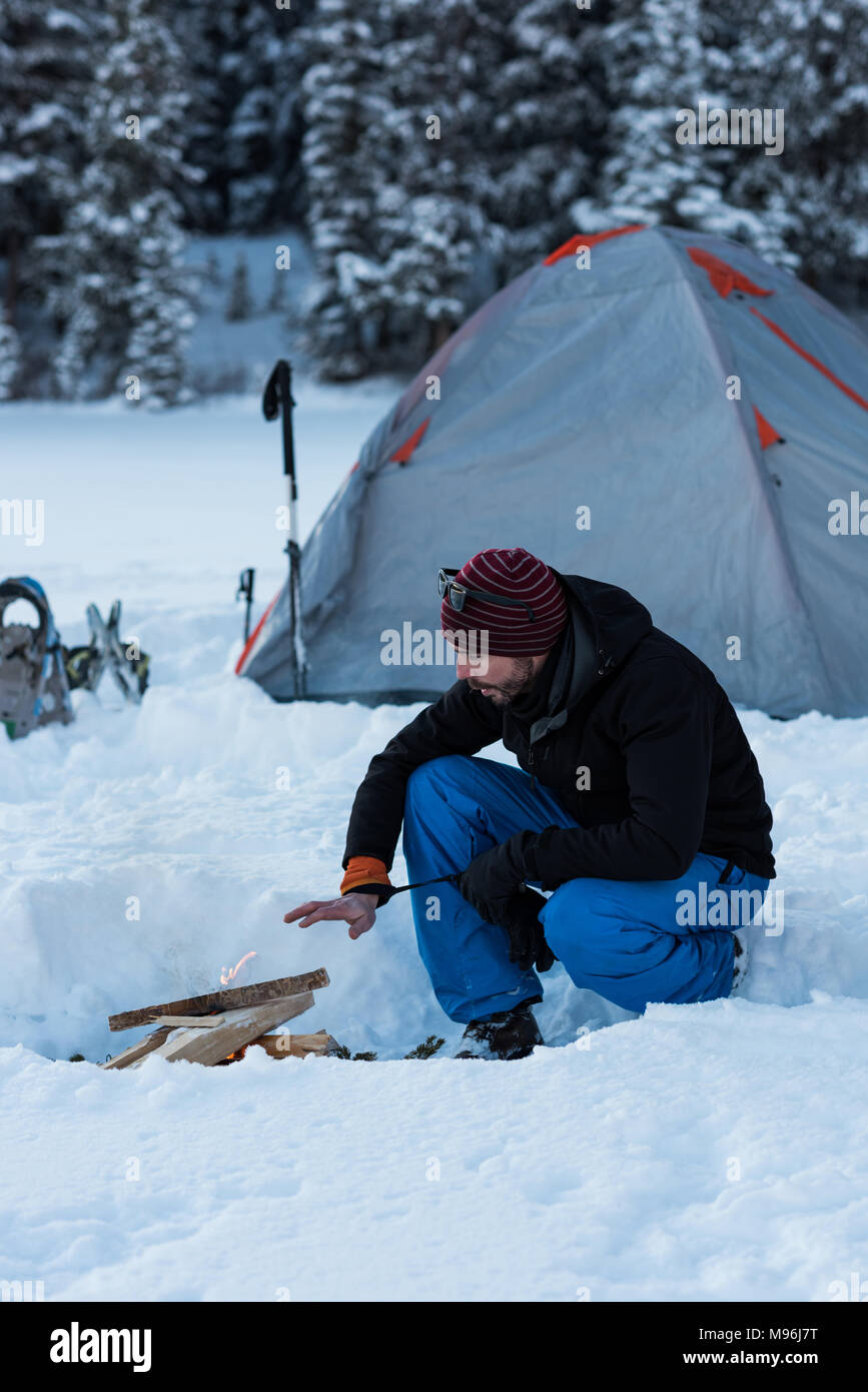 Man preparing bonfire near tent in snowy landscape Stock Photo