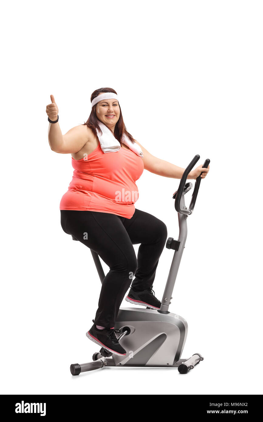 Overweight woman exercising on a stationary bike and making a thumb up gesture isolated on white background Stock Photo