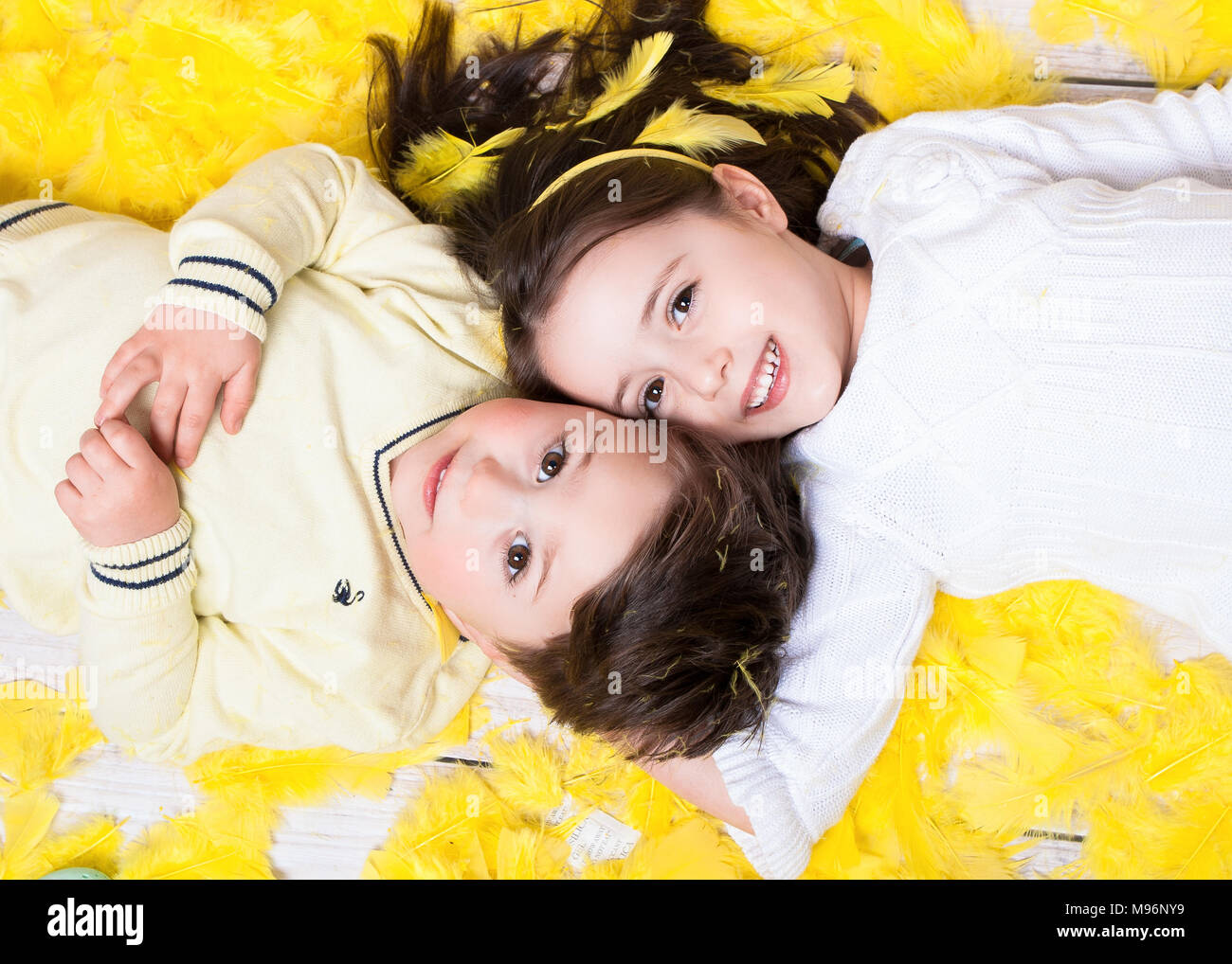 Girl and boy (4-6) lying on yellow feather smiling. Spring and Easter concept Stock Photo