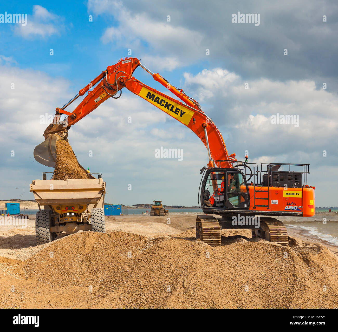 Excavator loading a dumper truck on a beach. Stock Photo
