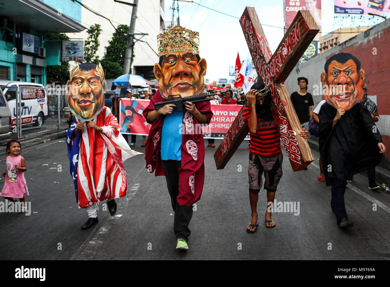 Manila, Philippines. 23rd March, 2018. A protester carries a cross while activists wearing several Duterte masks mock and hit him as they March towards Mendiola bridge in Manila. Activists slammed Duterte for the alleged double standard in his war on drugs, the crackdown on activists, and the recent designation of activists as terrorists according to the Malacanang. The March was held a few days before the Holy Week, with protesters carrying a cross to Mendiola, Manila. Credit: SOPA Images Limited/Alamy Live News Stock Photo