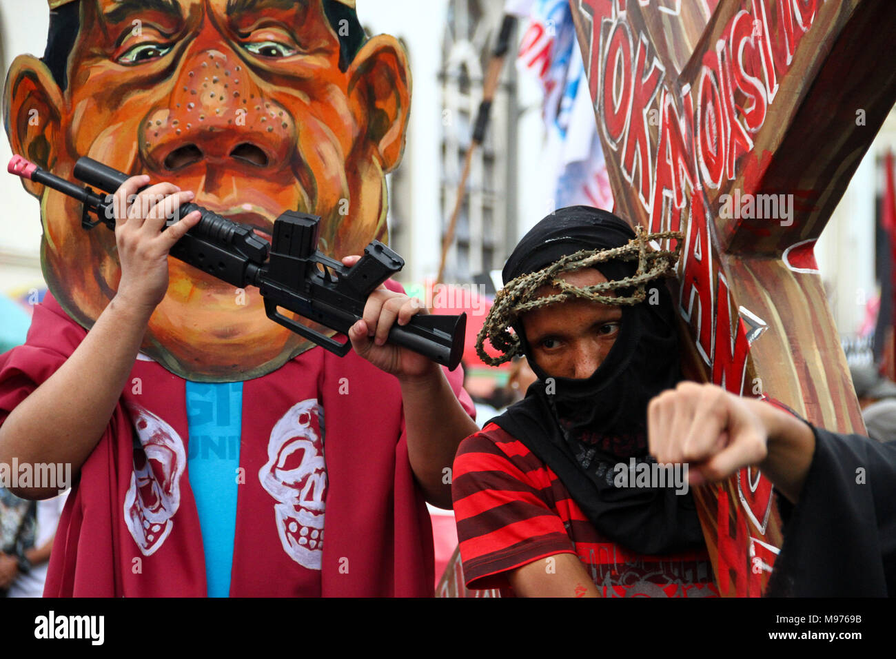 Manila, Philippines. 23rd March, 2018. A protester carries a cross while an activist wear a Duterte mask mock and hit him as they March towards Mendiola bridge in Manila. Activists slammed Duterte for the alleged double standard in his war on drugs, the crackdown on activists, and the recent designation of activists as terrorists according to the Malacanang. The March was held a few days before the Holy Week, with protesters carrying a cross to Mendiola, Manila. Credit: SOPA Images Limited/Alamy Live News Stock Photo
