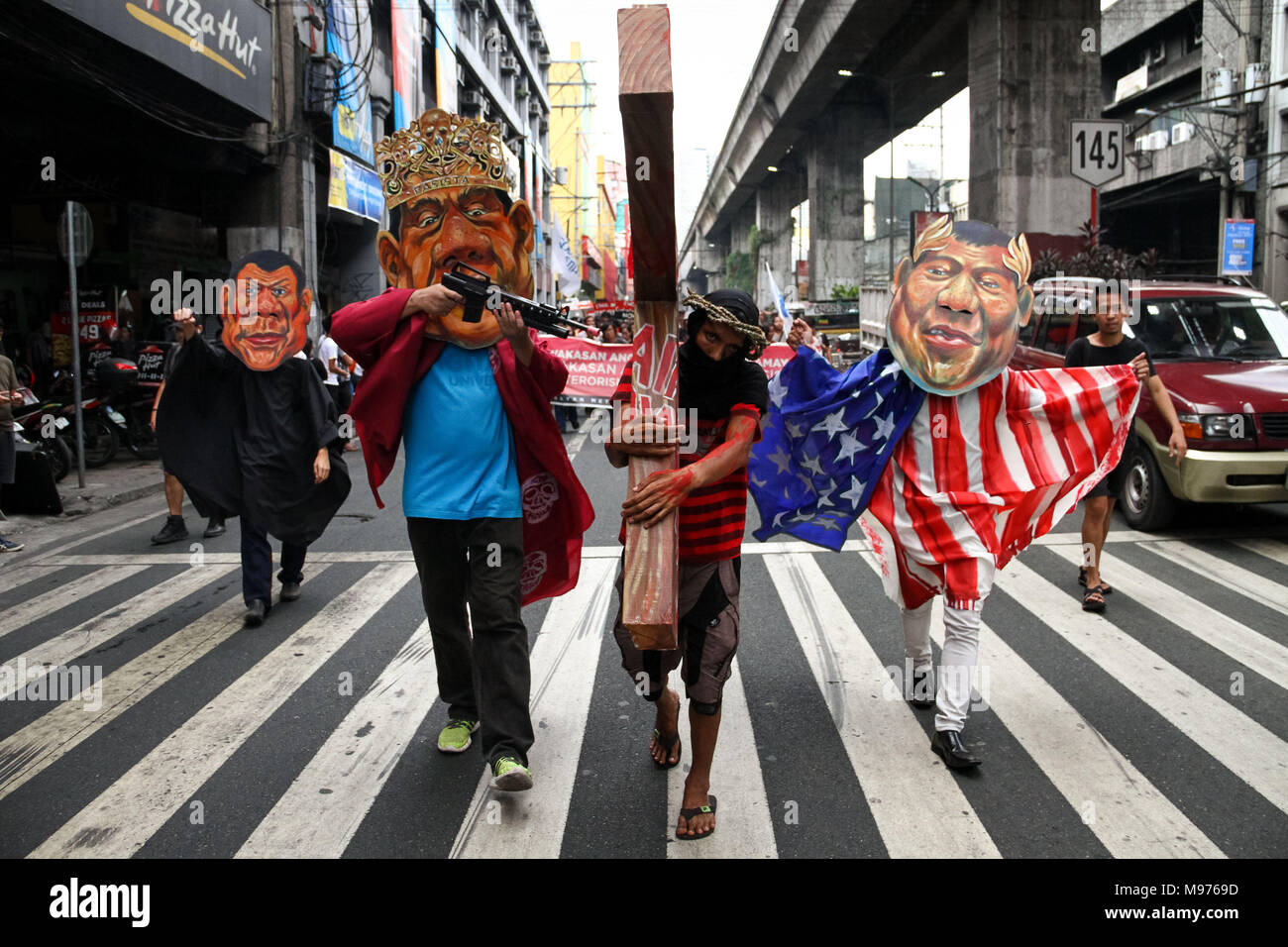 Manila, Philippines. 23rd March, 2018. A protester carries a cross while activists wearing several Duterte masks mock and hit him as they March towards Mendiola bridge in Manila. Activists slammed Duterte for the alleged double standard in his war on drugs, the crackdown on activists, and the recent designation of activists as terrorists according to the Malacanang. The March was held a few days before the Holy Week, with protesters carrying a cross to Mendiola, Manila. Credit: SOPA Images Limited/Alamy Live News Stock Photo