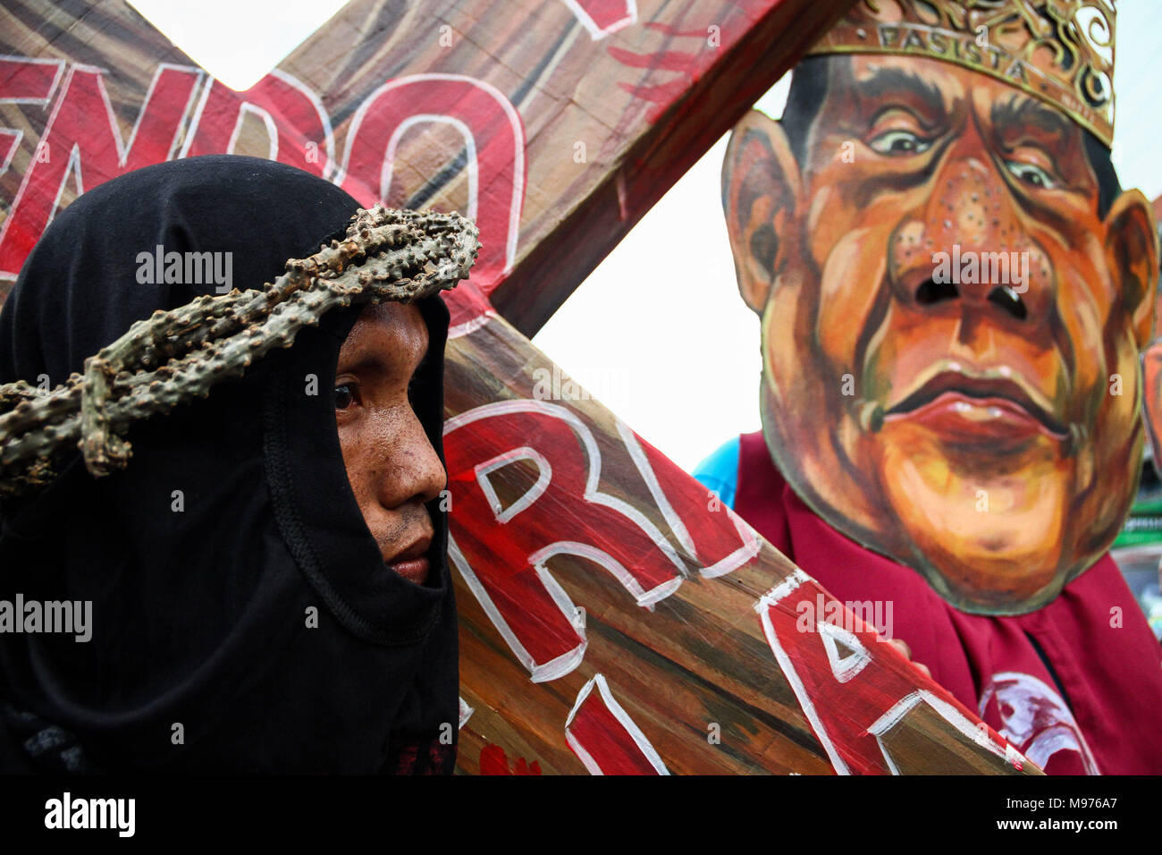 Manila, Philippines. 23rd March, 2018. A protester carries a cross while an activist wear a Duterte mask mock and hit him as they March towards Mendiola bridge in Manila. Activists slammed Duterte for the alleged double standard in his war on drugs, the crackdown on activists, and the recent designation of activists as terrorists according to the Malacanang. The March was held a few days before the Holy Week, with protesters carrying a cross to Mendiola, Manila. Credit: SOPA Images Limited/Alamy Live News Stock Photo