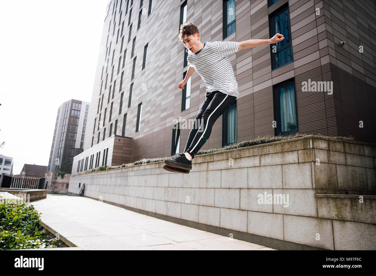 Young freerunner is jumping down from a wall in the city. Stock Photo