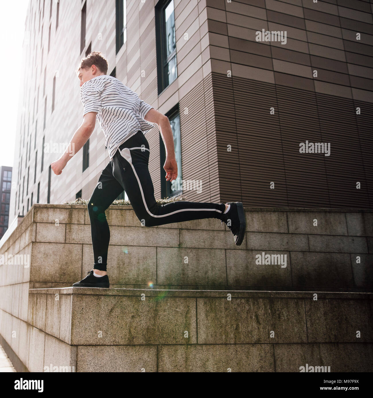 Young freerunner is doing stunts in the city. He is running along a ...