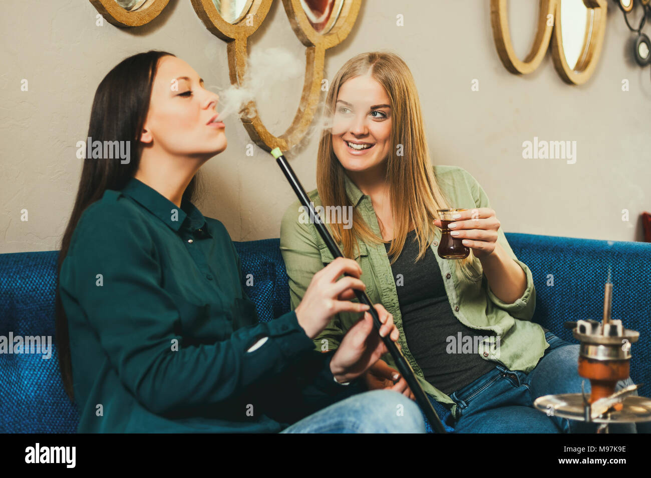 Two happy women are sitting in shisha bar and smoking nargile Stock Photo