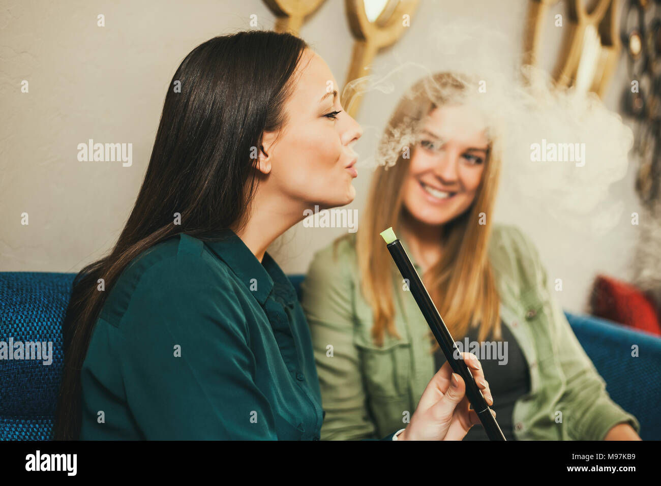 Two happy women are sitting in shisha bar and smoking nargile Stock Photo