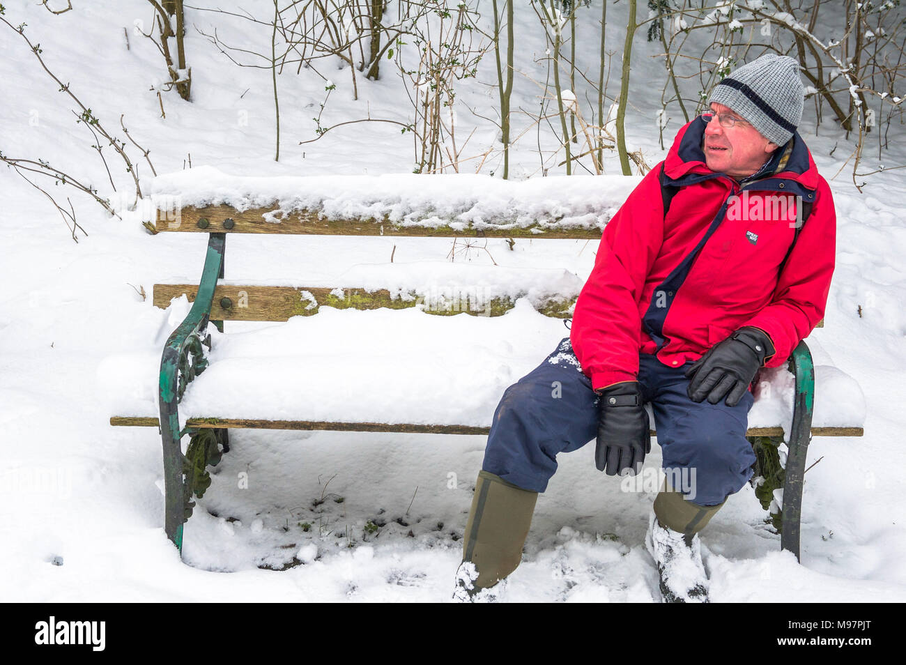 Man with winter clothing sitting on a snow covered bench. Stock Photo