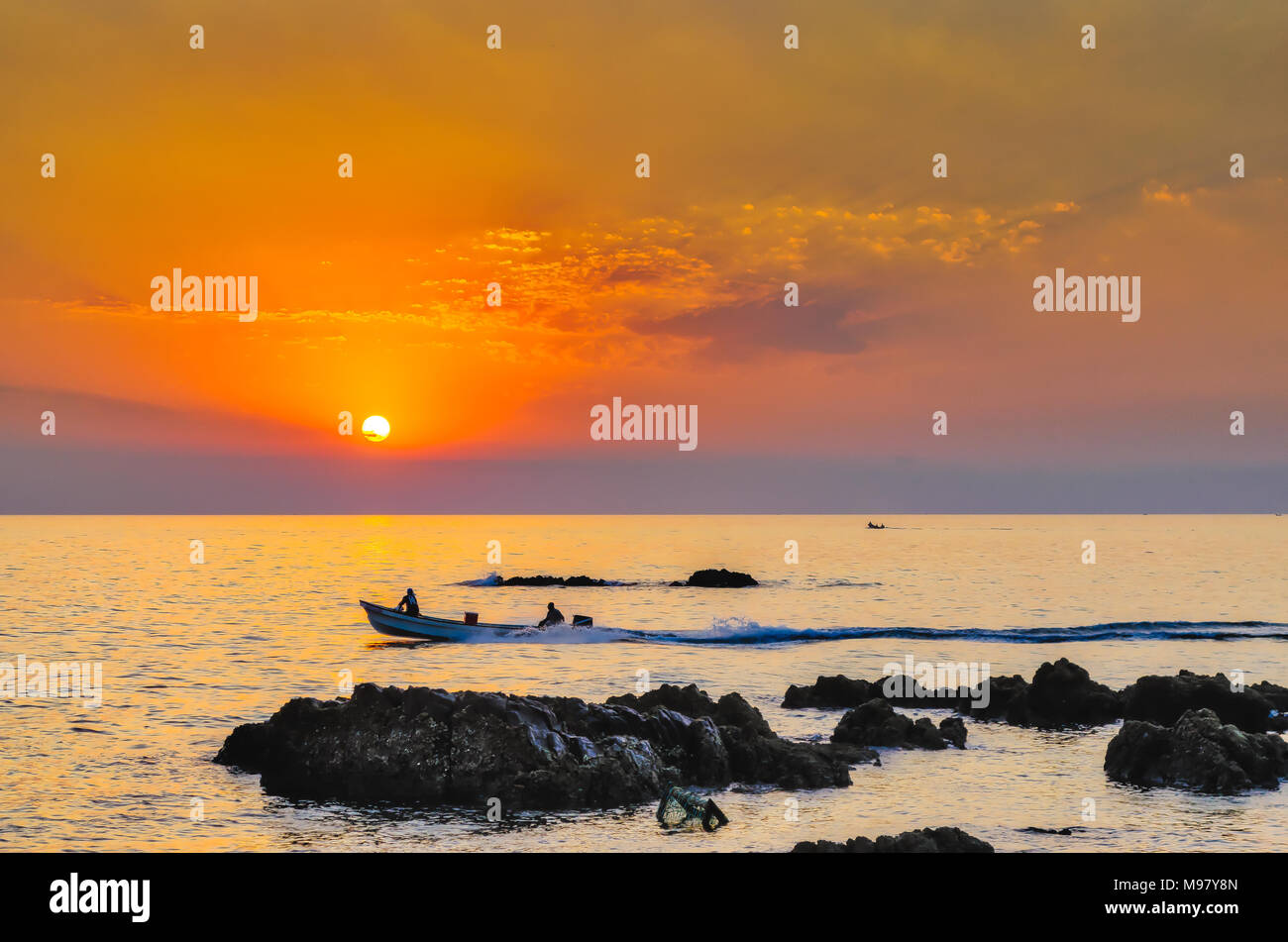 Silhouette of fishermen in the boat going for fishing during sunrise with orange sky for company! Stock Photo