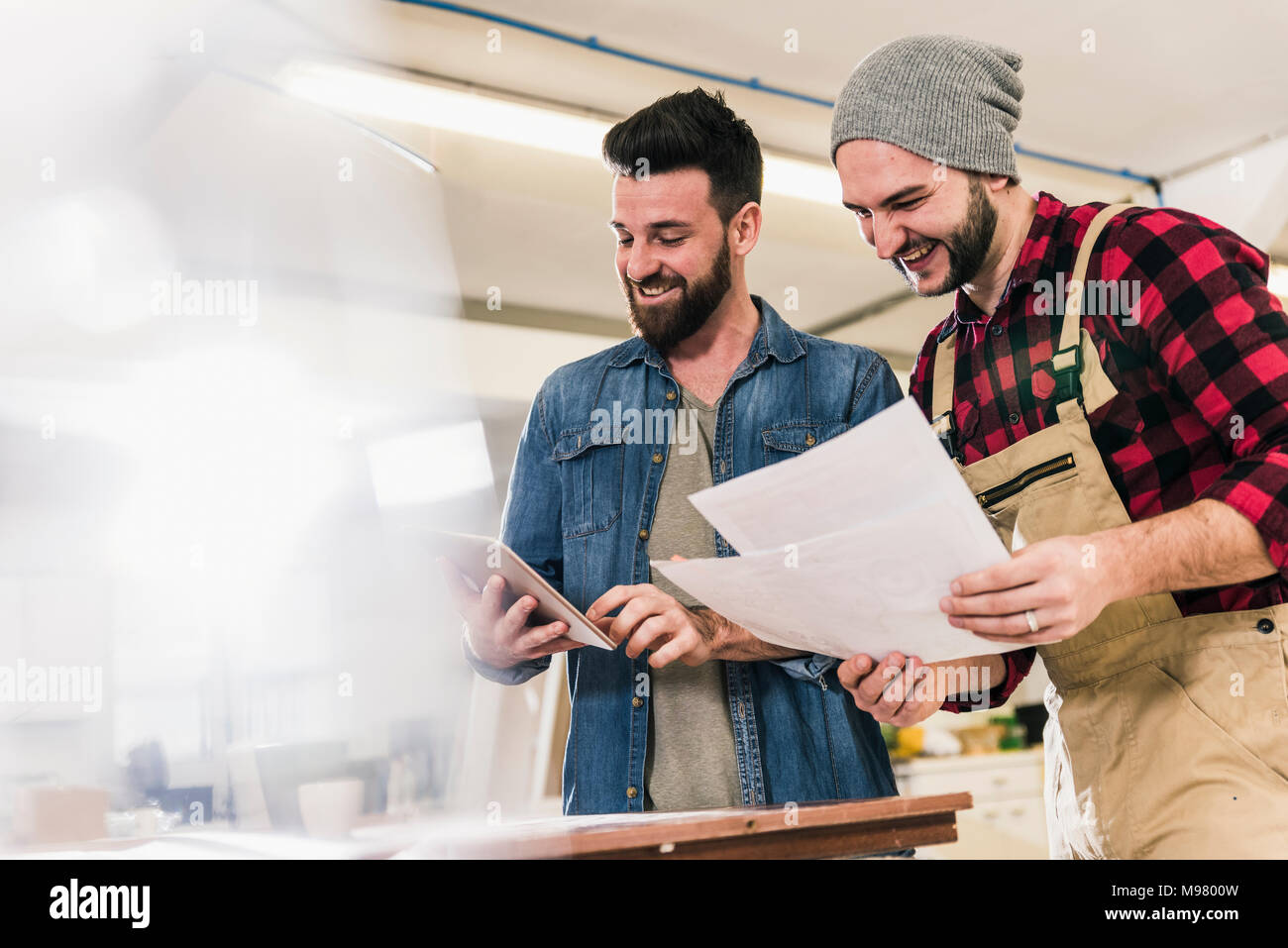 Two happy men with tablet looking at draft in workshop Stock Photo