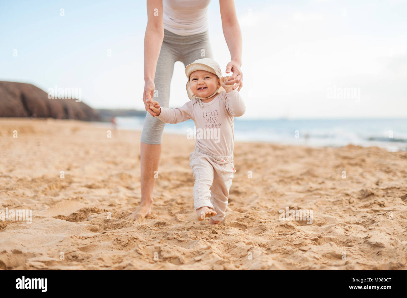 Mother helping little daughter walking on the beach Stock Photo