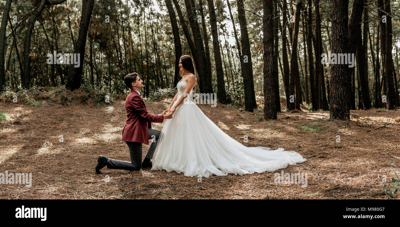 Man kneeling making a marriage proposal to happy bride in forest Stock Photo