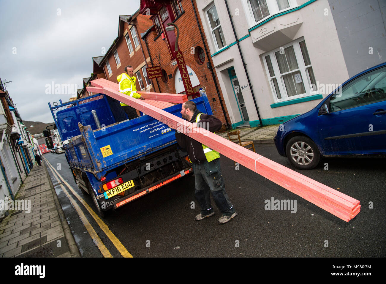 A delivery of wooden roofing timbers being unloaded by two men, wearing