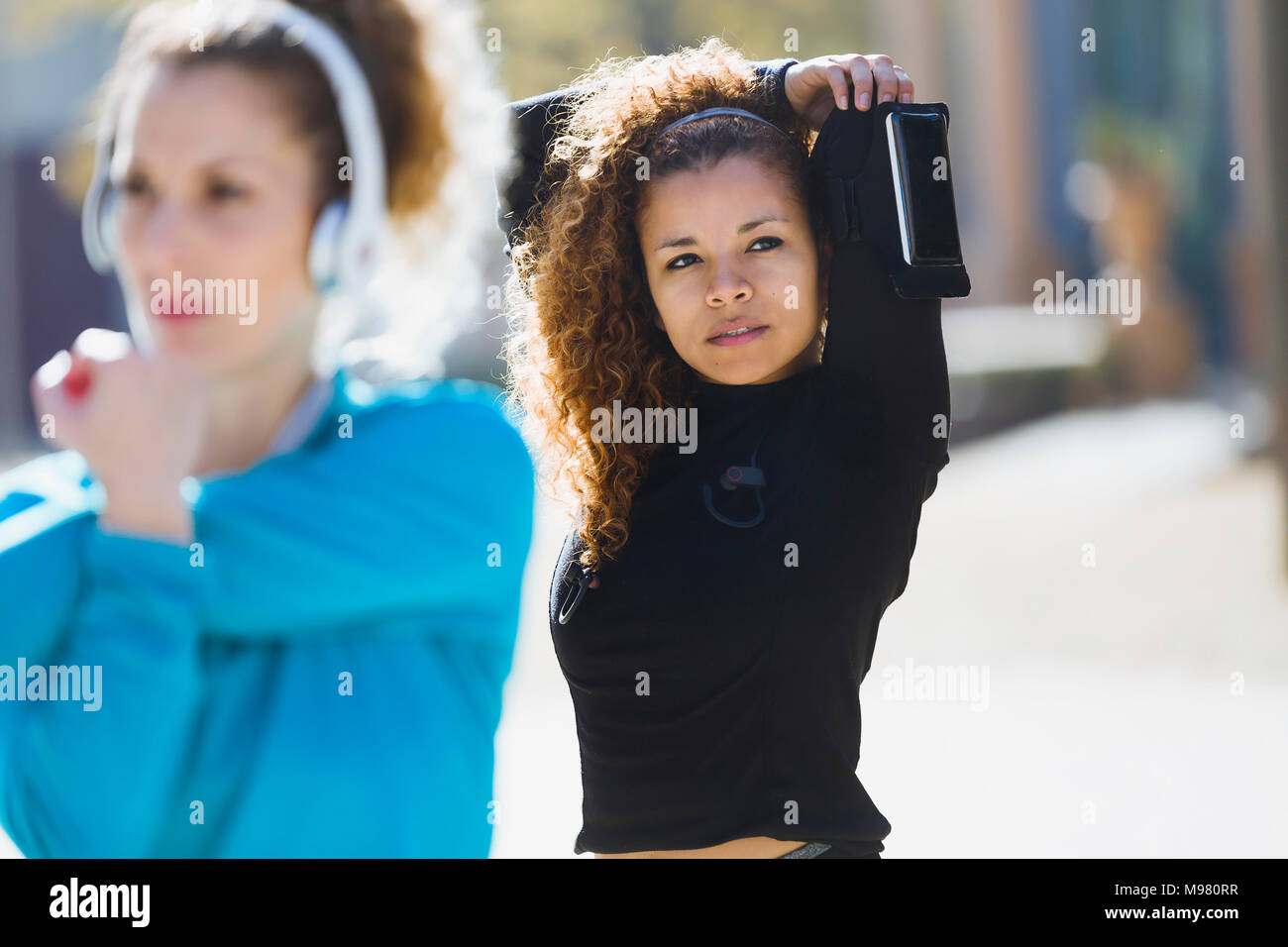 Two focused sportive young women stretching listening to music Stock Photo