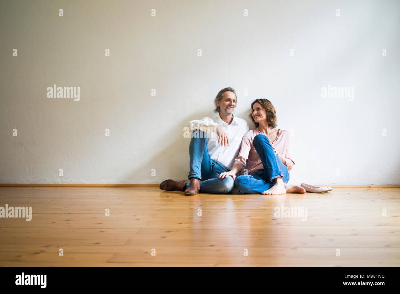 Smiling mature couple sitting on floor in empty room Stock Photo
