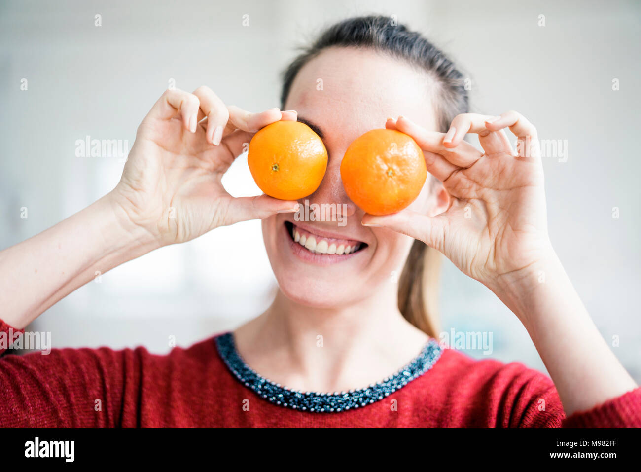 Laughing woman covering her eyes with oranges Stock Photo