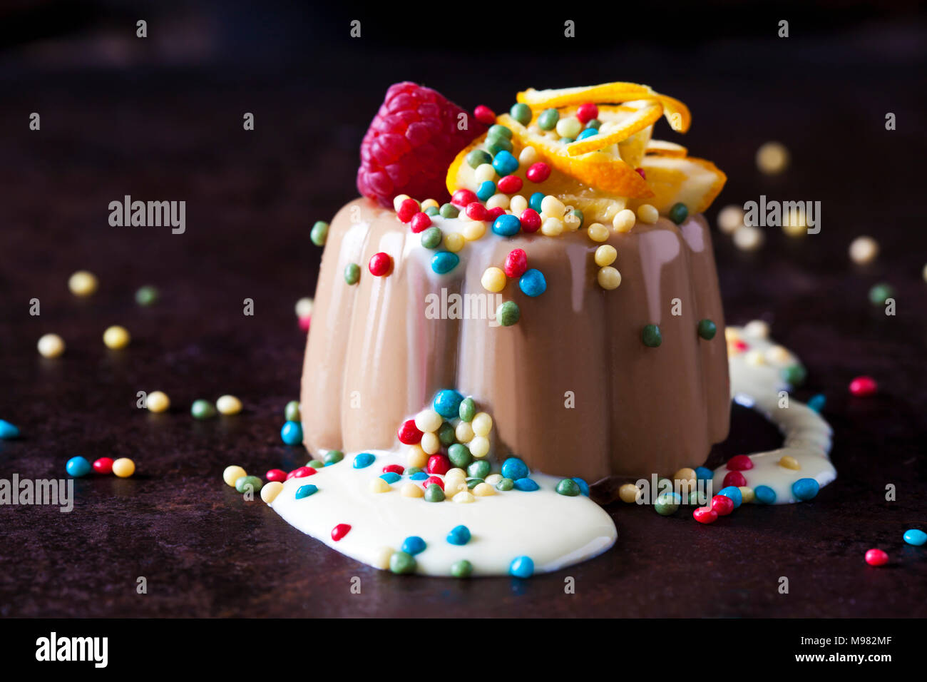 Chocolate pudding and vanilla sauce garnished with raspberry, orange and sugar beads Stock Photo