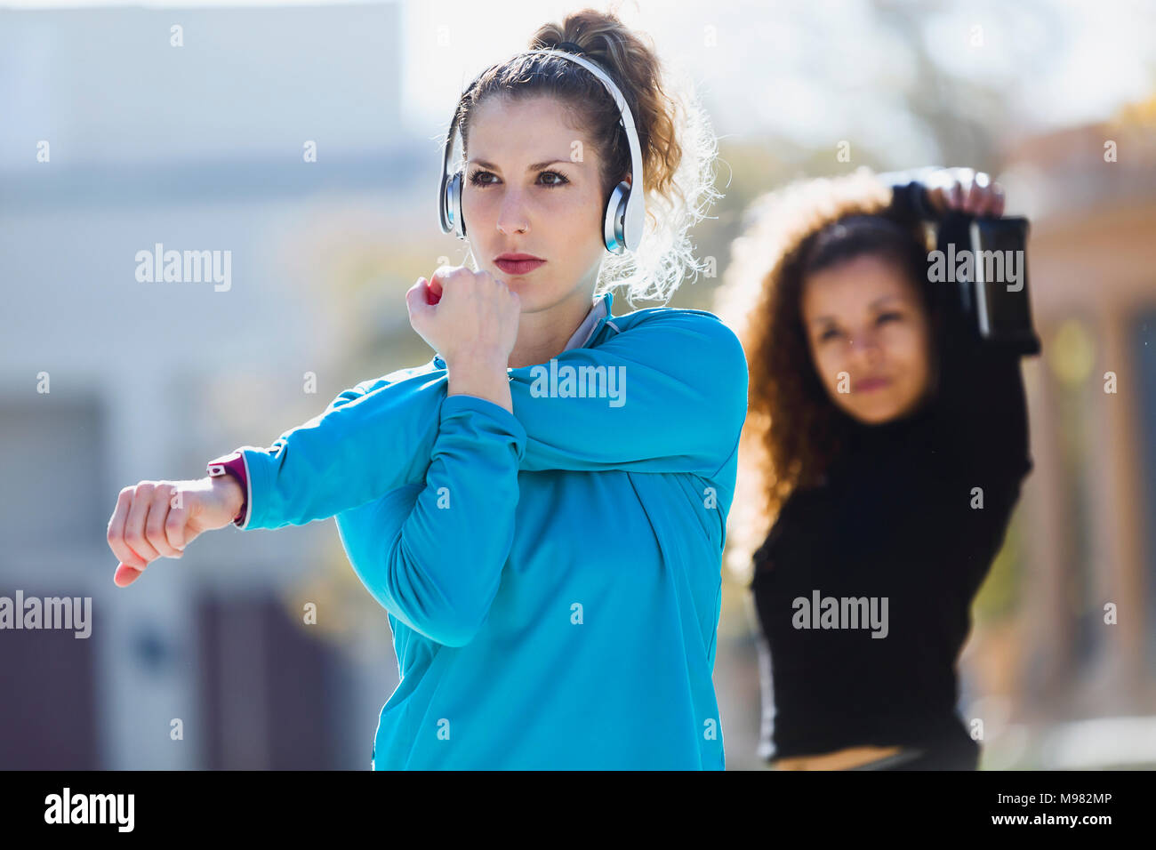 Two focused sportive young women stretching listening to music Stock Photo