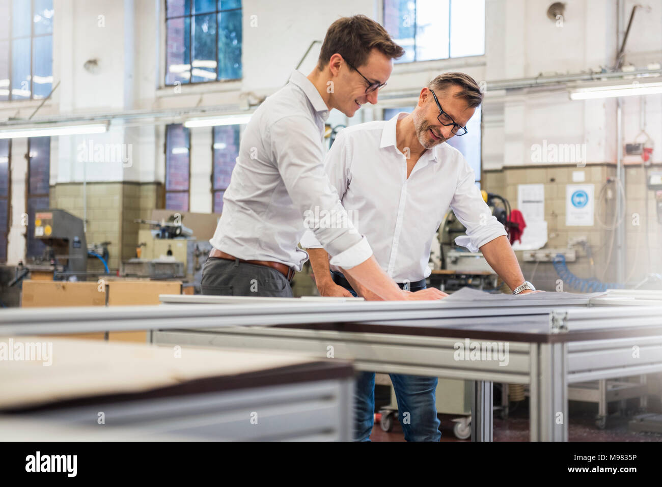 Two smiling businessmen in factory looking at plan Stock Photo - Alamy