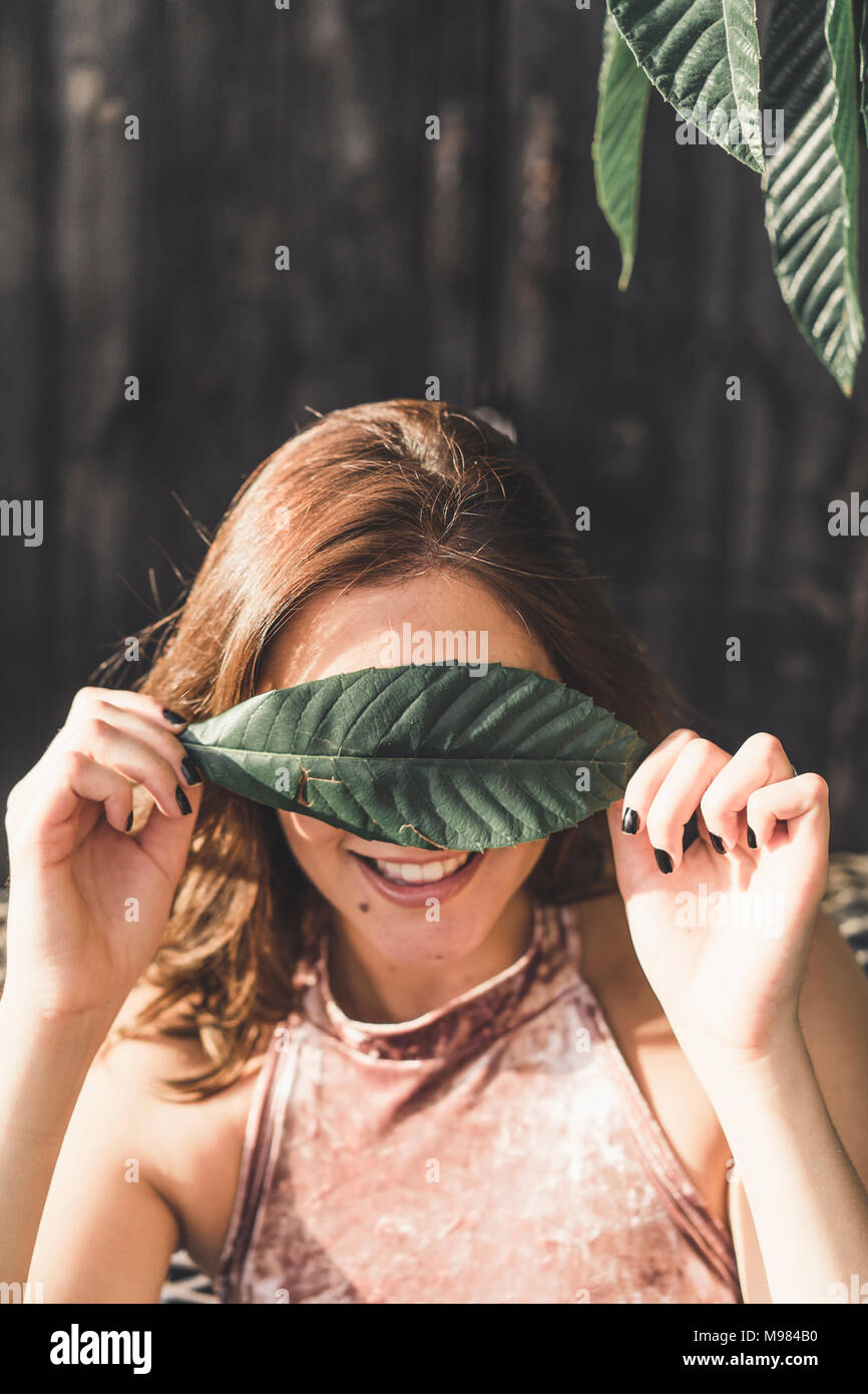 Smiling young woman covering eyes with a leaf Stock Photo - Alamy