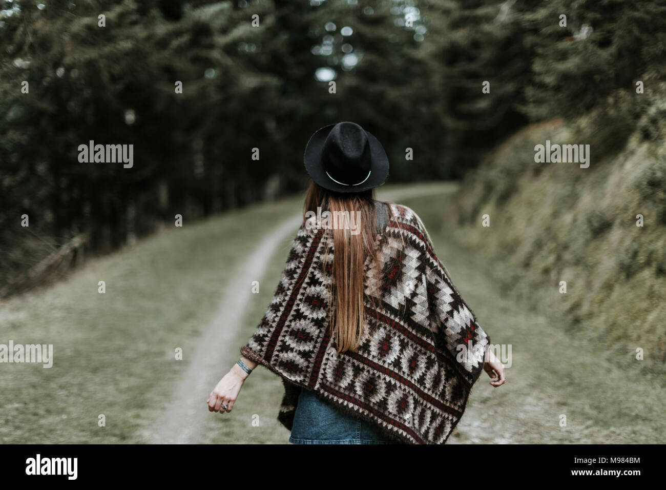 Back view of fashionable young woman wearing hat and poncho in nature Stock Photo