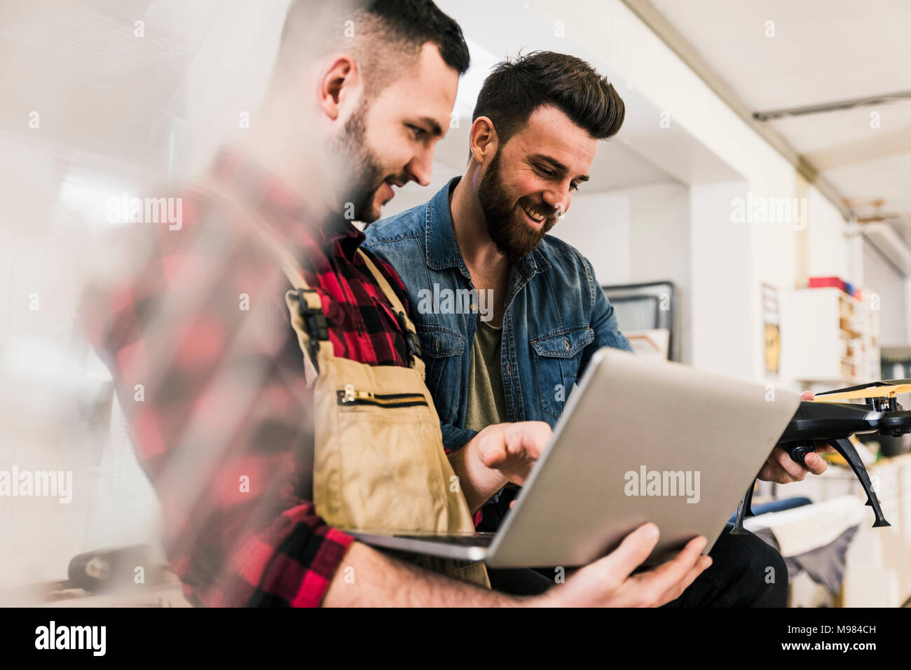 Two smiling men with laptop and drone in workshop Stock Photo