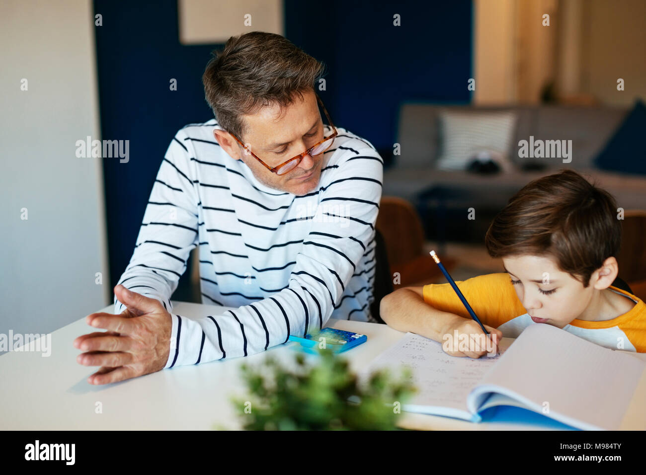 Father watching son doing homework at table Stock Photo - Alamy