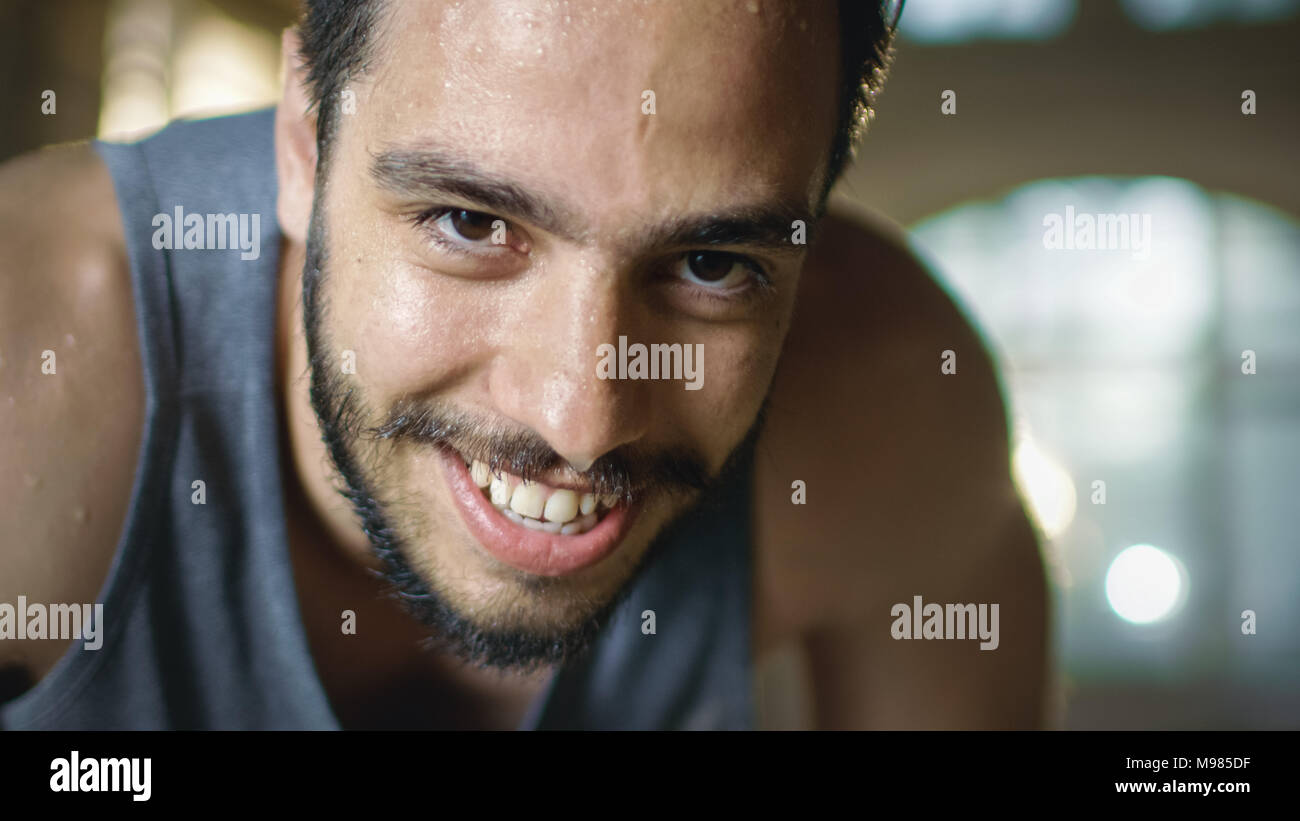 Exhausted Bend Muscular Man Looks into Camera and Rests After Intensive Workout. He's In a Gym and Covered in Sweat. He Tries to Catch a Breath. Stock Photo