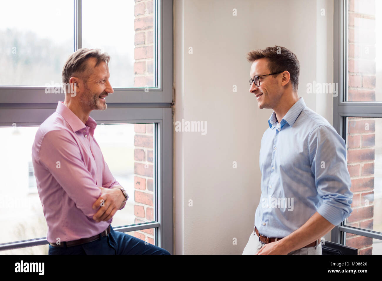 Two smiling businessmen talking at the window Stock Photo - Alamy