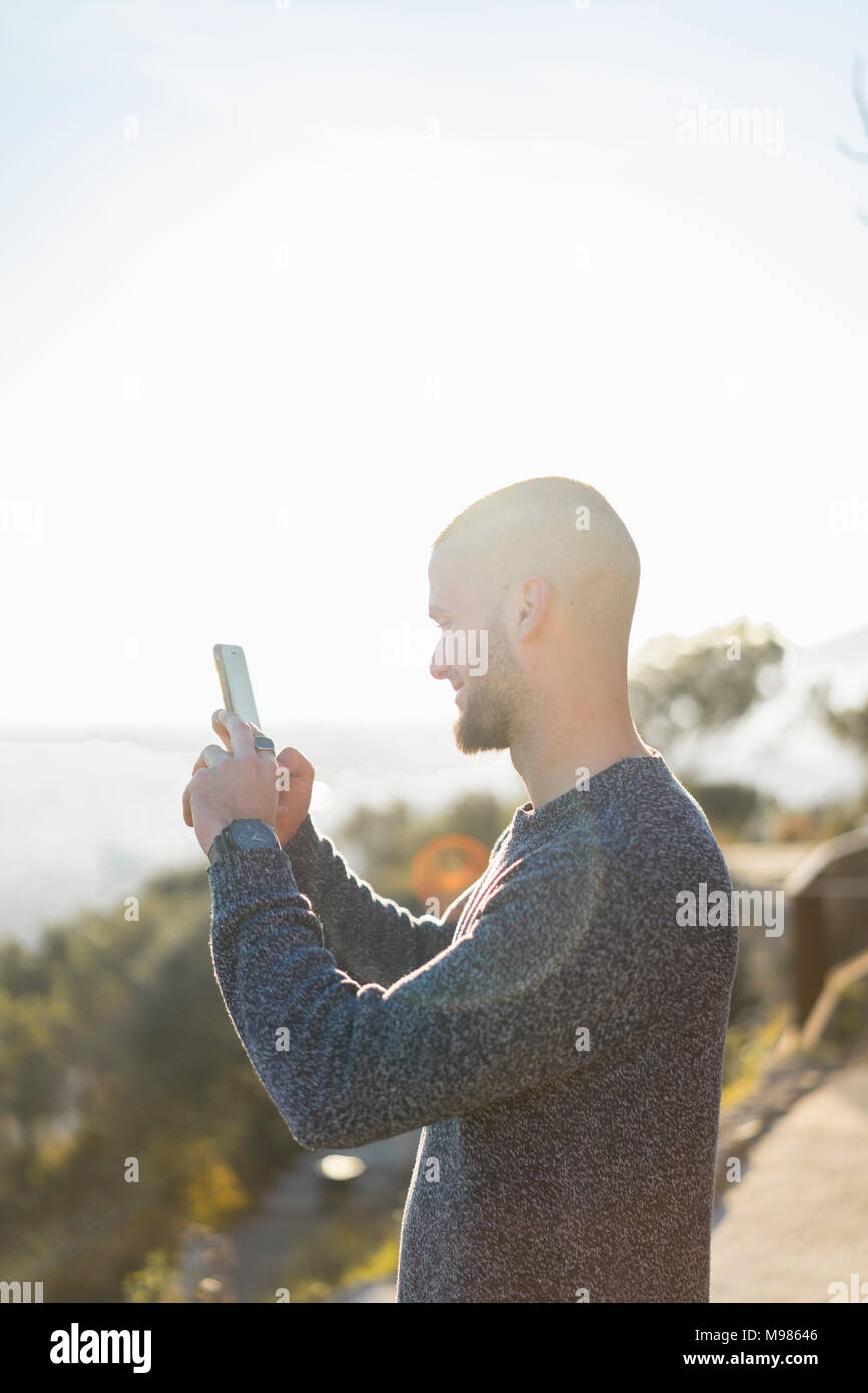 Smiling young man holding cell phone in backlight Stock Photo