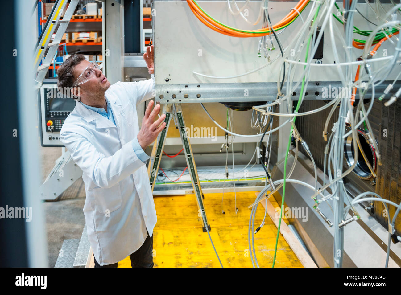 Man wearing lab coat and safety goggles examining at machine Stock Photo