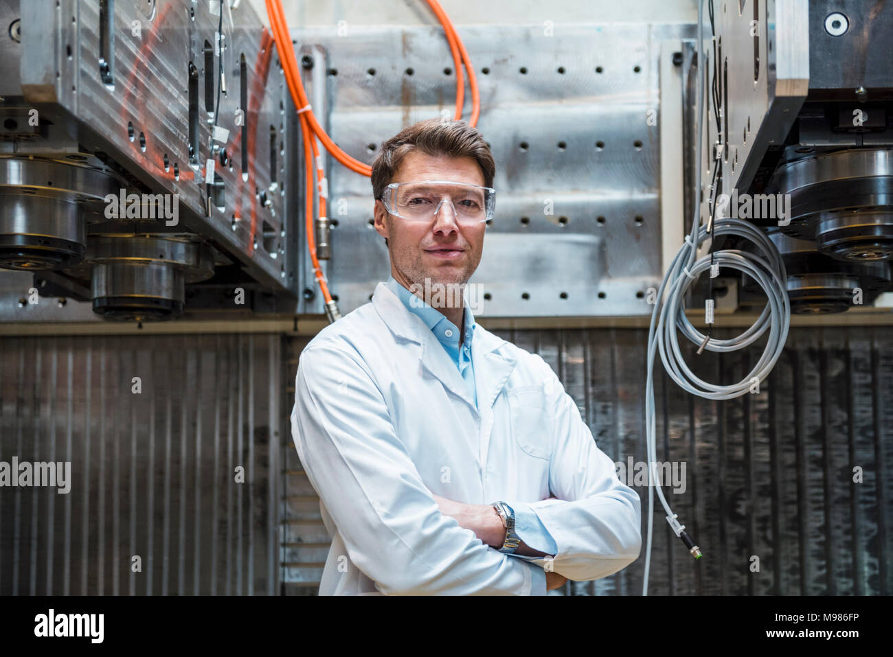 Portrait of man wearing lab coat and safety goggles at machine Stock Photo