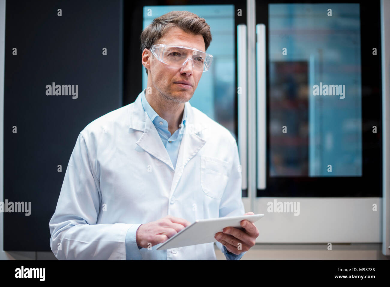 Portrait of man wearing lab coat and safety goggles holding tablet at