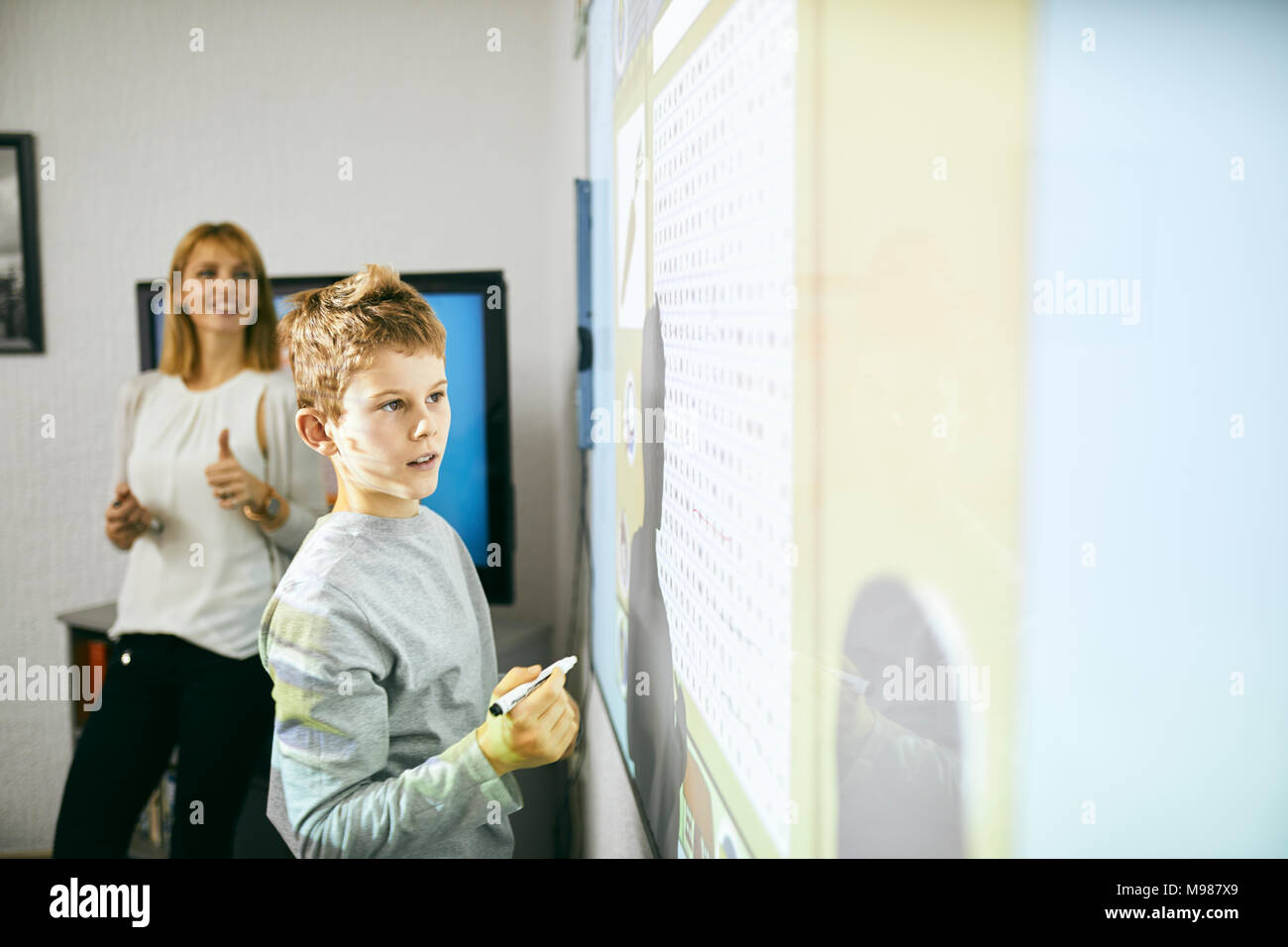 Student in class at interactive whiteboard with teacher in background Stock Photo
