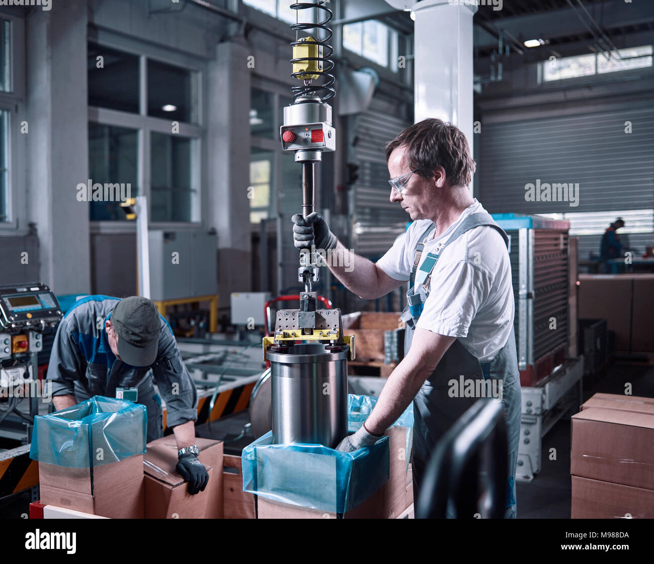 Worker using indoor crane for lifting metalsocket from cardboard box Stock Photo