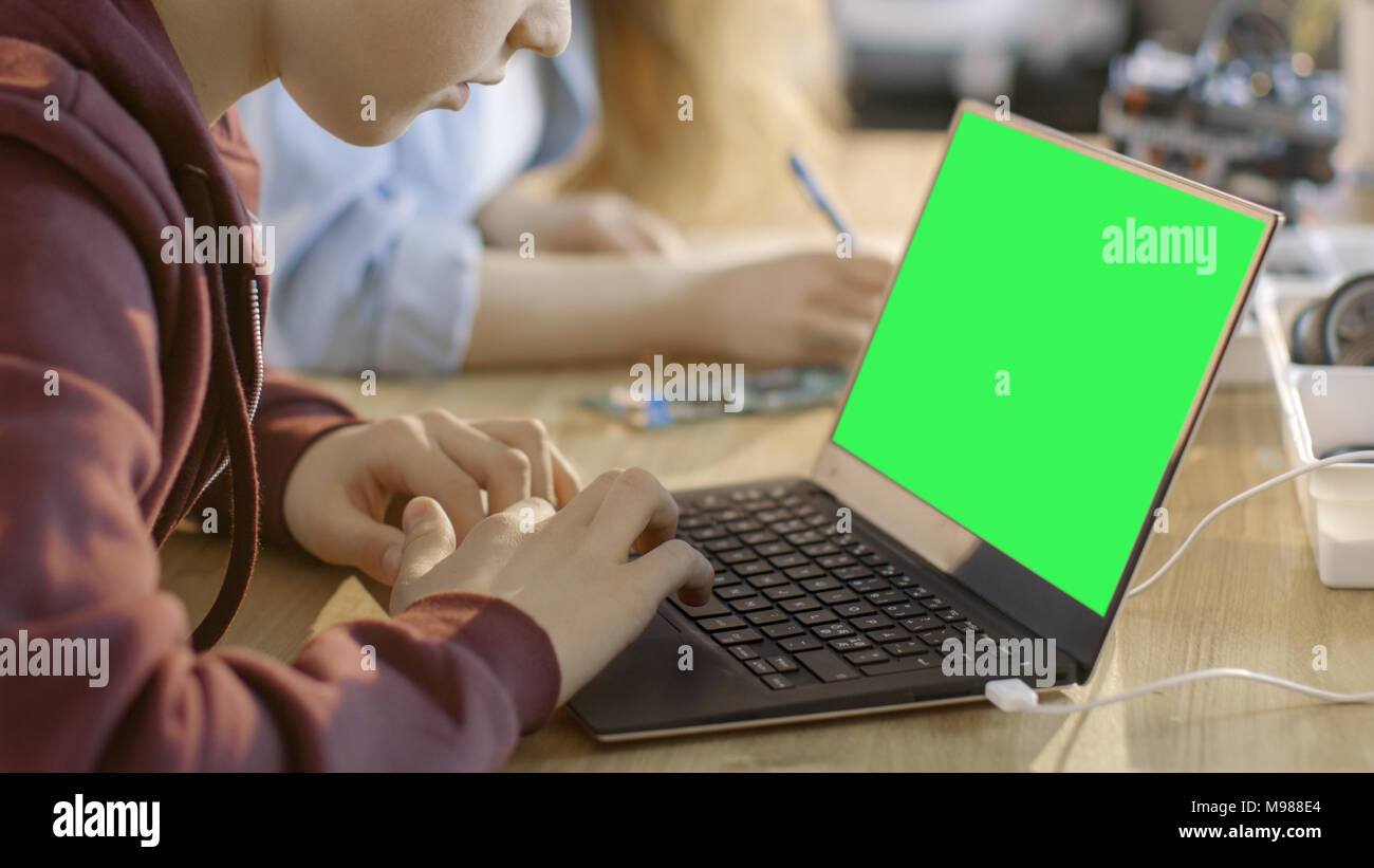 Smart Young Boy Works on a Laptop with Mock-up Green Screen in His Computer Science Class. Stock Photo