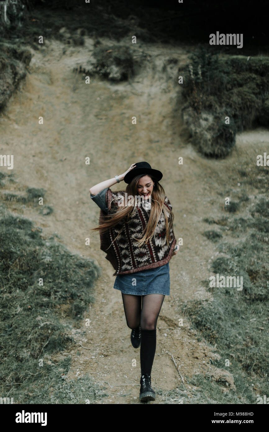 Fashionable young woman wearing hat and poncho running downhill Stock Photo