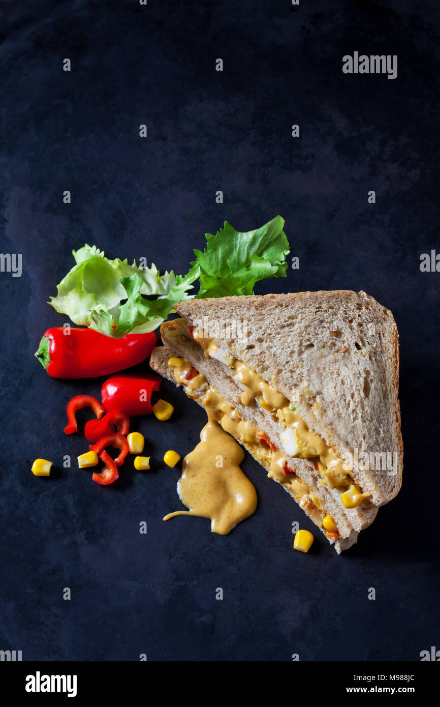 Chicken sandwich with corn, pepperoni and curry sauce on dark ground